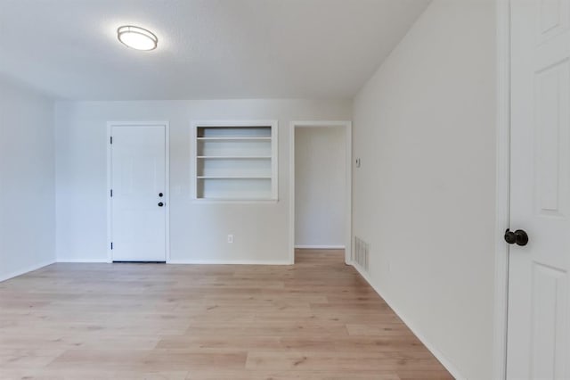 unfurnished room with built in shelves and light hardwood / wood-style flooring