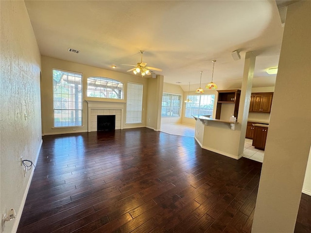 unfurnished living room featuring a fireplace, ceiling fan, dark wood-type flooring, and a healthy amount of sunlight