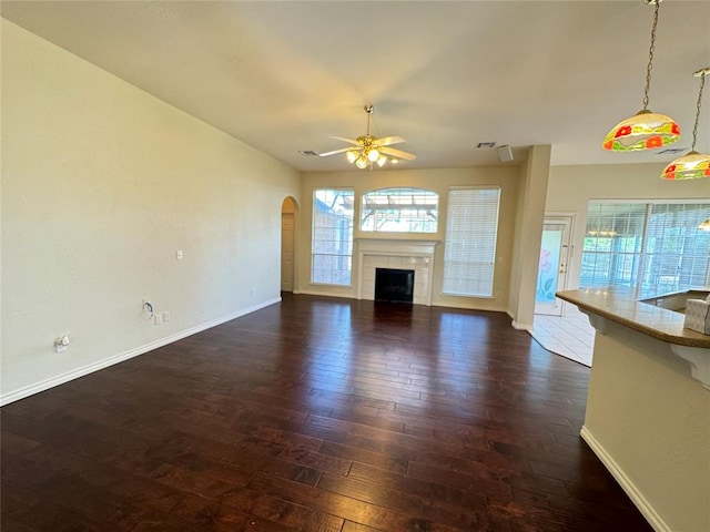 unfurnished living room featuring a tile fireplace, dark hardwood / wood-style floors, and ceiling fan