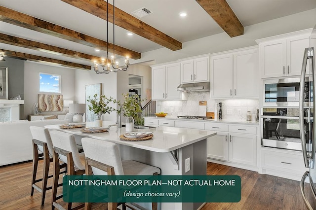 kitchen with appliances with stainless steel finishes, decorative light fixtures, white cabinetry, and an island with sink