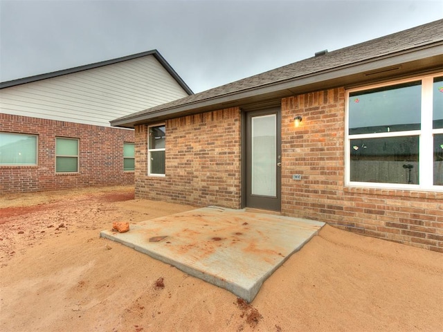 exterior space featuring a patio, brick siding, and roof with shingles