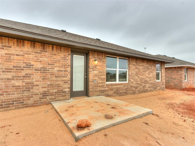 exterior space featuring a patio area, roof with shingles, and brick siding