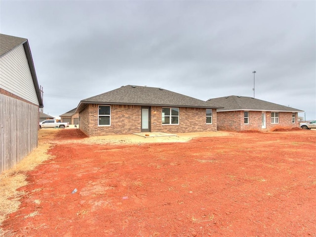 back of property featuring a shingled roof, brick siding, and a patio