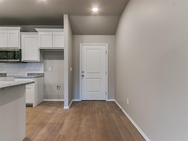 kitchen featuring light stone countertops, white cabinetry, backsplash, and stainless steel microwave