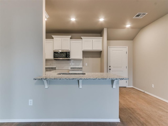 kitchen with stainless steel microwave, visible vents, a kitchen bar, and white cabinetry