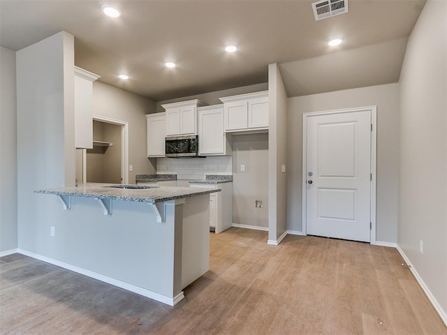 kitchen with a breakfast bar, white cabinetry, visible vents, light stone countertops, and stainless steel microwave