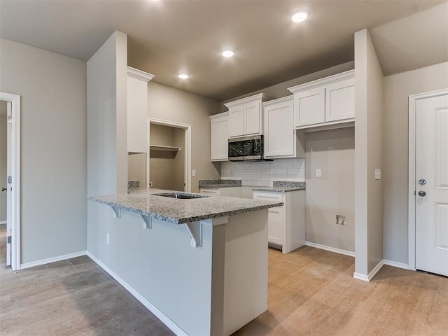 kitchen featuring stainless steel microwave, white cabinetry, light stone countertops, a peninsula, and a kitchen bar