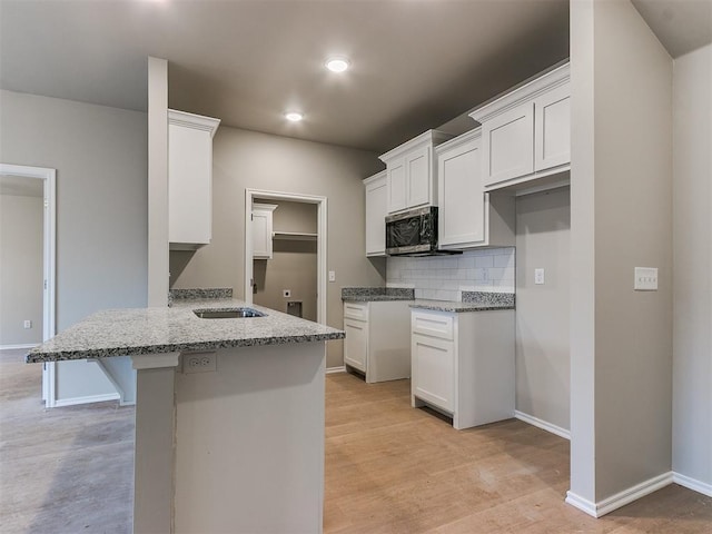 kitchen with a peninsula, stainless steel microwave, a kitchen bar, and light stone countertops