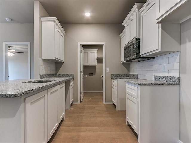 kitchen featuring white cabinetry, backsplash, light wood finished floors, and light stone countertops