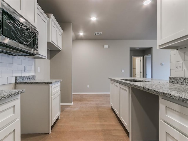 kitchen featuring white cabinets, stainless steel microwave, backsplash, and light stone counters