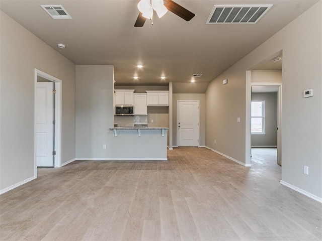 interior space featuring a ceiling fan, stainless steel microwave, visible vents, and white cabinetry