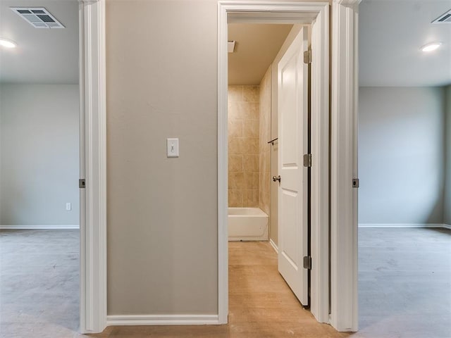 corridor with light wood-style floors, visible vents, and baseboards