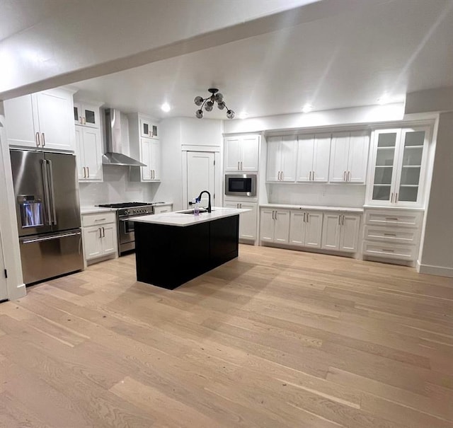 kitchen featuring white cabinets, wall chimney exhaust hood, stainless steel appliances, and a kitchen island with sink