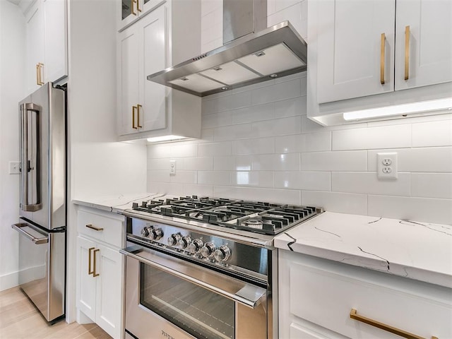 kitchen with light stone countertops, white cabinets, high end appliances, and wall chimney range hood