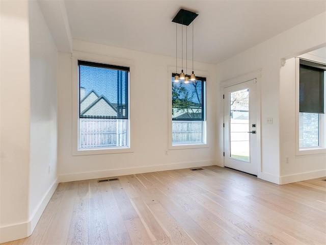 unfurnished dining area featuring a chandelier, a healthy amount of sunlight, and light hardwood / wood-style flooring