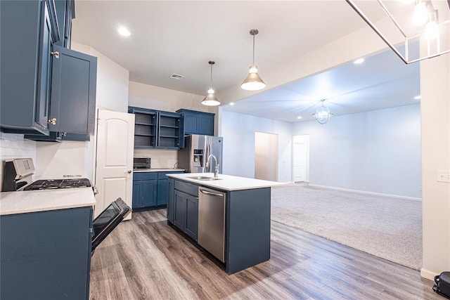 kitchen with appliances with stainless steel finishes, decorative light fixtures, an island with sink, sink, and blue cabinetry