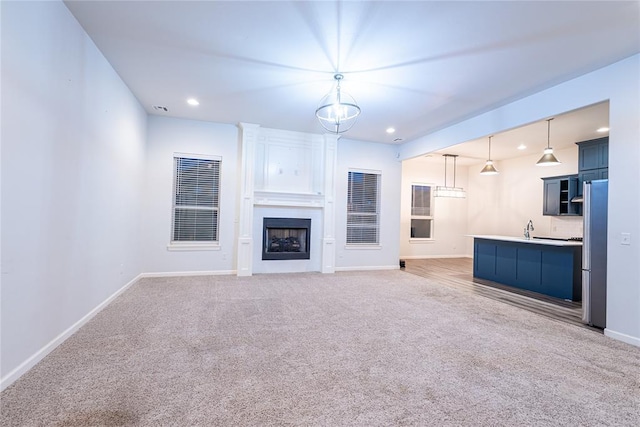 unfurnished living room with a fireplace, carpet floors, sink, and a chandelier