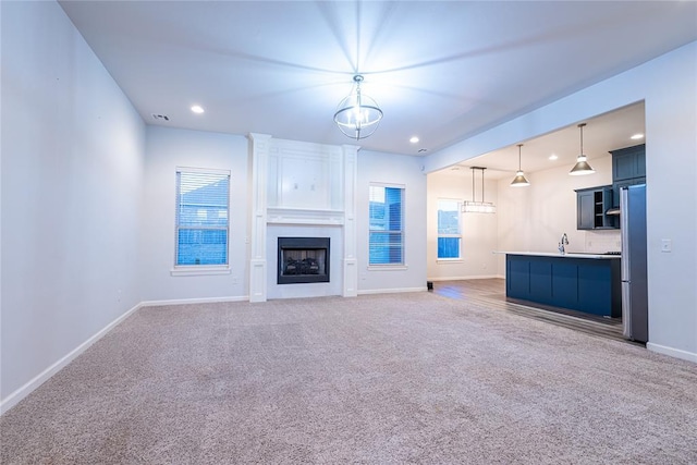 unfurnished living room with a notable chandelier, carpet flooring, a wealth of natural light, and a large fireplace