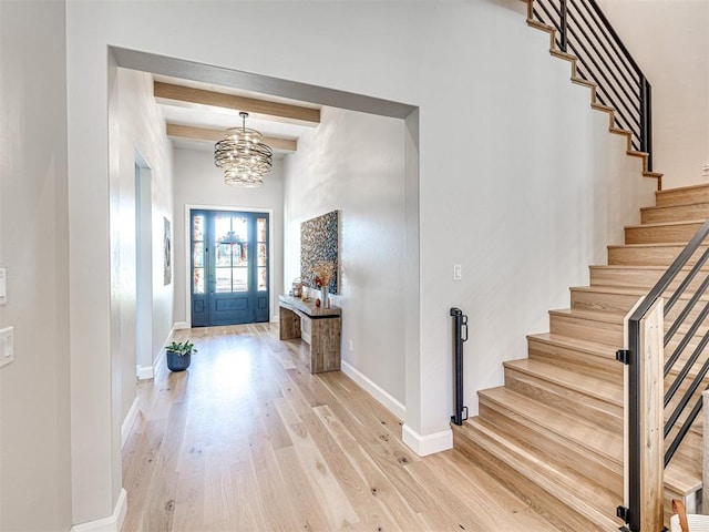 foyer entrance featuring beamed ceiling, light wood-type flooring, and an inviting chandelier