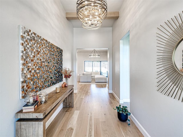 hallway with beamed ceiling, a towering ceiling, a chandelier, and light hardwood / wood-style flooring