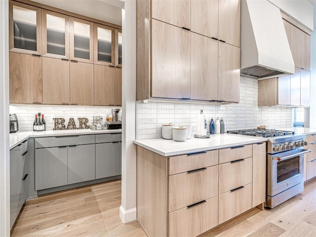 kitchen featuring light brown cabinets, tasteful backsplash, custom range hood, and high end range