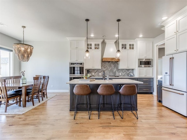 kitchen with stainless steel appliances, an island with sink, pendant lighting, white cabinets, and custom exhaust hood