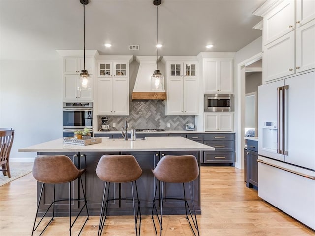 kitchen with white cabinets, a center island with sink, hanging light fixtures, appliances with stainless steel finishes, and light hardwood / wood-style floors