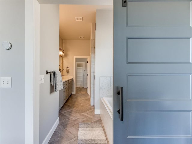 bathroom with tiled tub, vanity, and parquet flooring