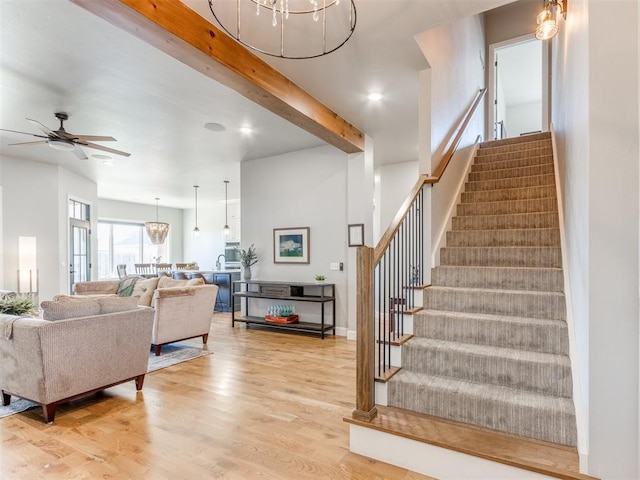 stairway featuring beamed ceiling, wood-type flooring, and ceiling fan with notable chandelier