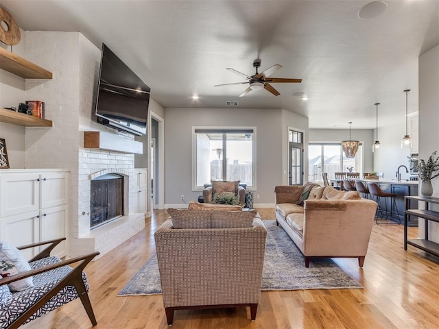 living room featuring ceiling fan, light hardwood / wood-style floors, sink, and a brick fireplace