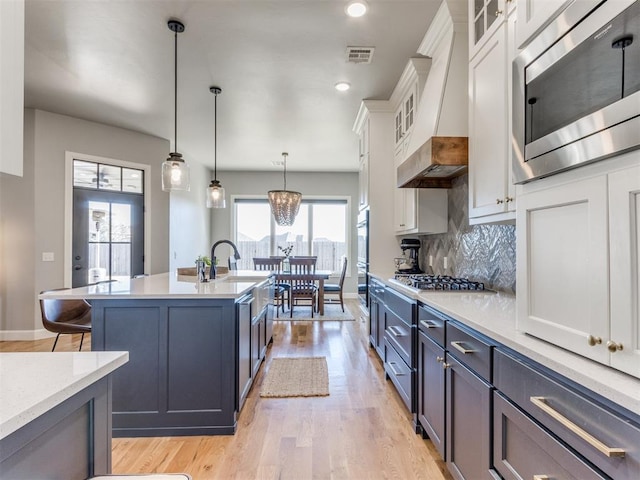 kitchen featuring premium range hood, appliances with stainless steel finishes, pendant lighting, white cabinets, and light wood-type flooring