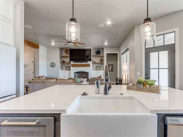 kitchen featuring dishwasher, a center island with sink, sink, light stone countertops, and decorative light fixtures