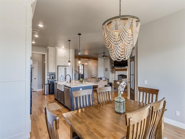 dining room featuring ceiling fan with notable chandelier, light wood-type flooring, and sink