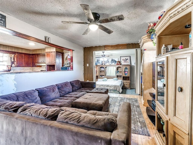 living room with a textured ceiling, light hardwood / wood-style floors, ceiling fan, and wooden walls