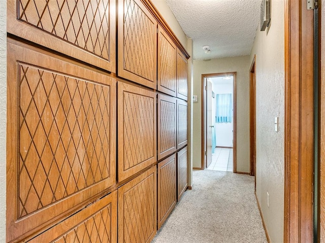 hallway with light colored carpet and a textured ceiling