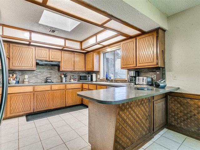 kitchen with kitchen peninsula, light tile patterned floors, a skylight, and tasteful backsplash