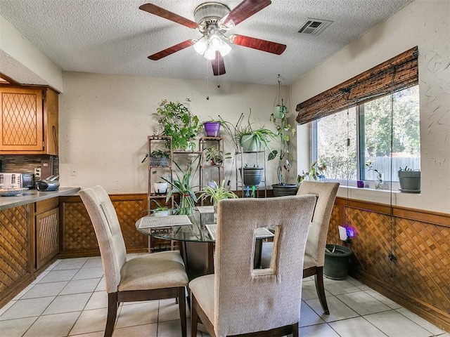 dining space featuring ceiling fan, wood walls, light tile patterned flooring, and a textured ceiling