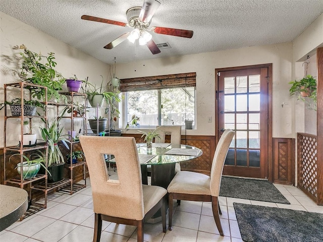 dining space with light tile patterned flooring, a textured ceiling, ceiling fan, and wood walls