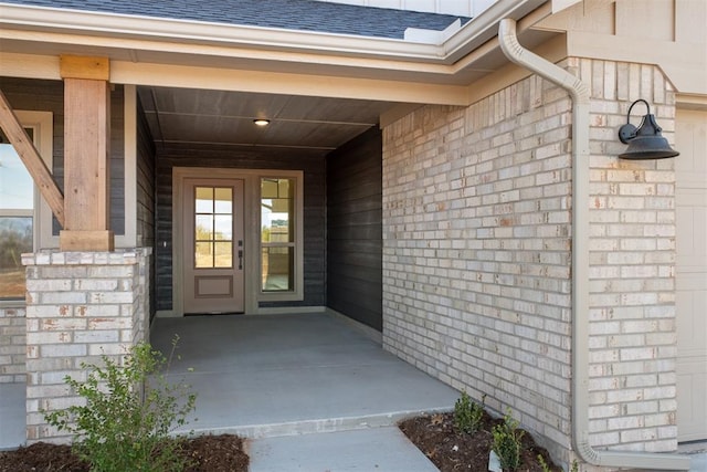 property entrance featuring a shingled roof and brick siding