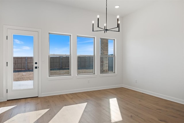 unfurnished dining area with a chandelier, baseboards, and light wood finished floors