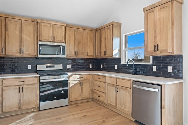 kitchen with light wood finished floors, stainless steel appliances, tasteful backsplash, light countertops, and a sink