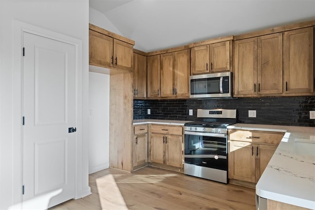 kitchen with tasteful backsplash, appliances with stainless steel finishes, brown cabinetry, light wood-style floors, and vaulted ceiling