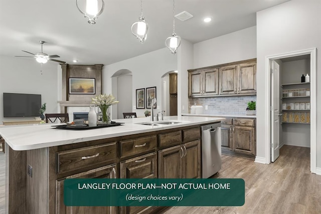 kitchen featuring ceiling fan, a large fireplace, light hardwood / wood-style flooring, stainless steel dishwasher, and a center island with sink