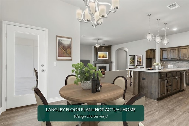 dining space with ceiling fan with notable chandelier, a large fireplace, light hardwood / wood-style floors, and sink