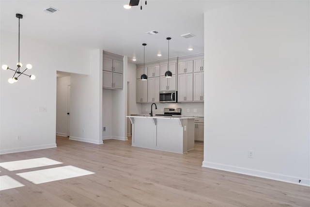 kitchen with hanging light fixtures, appliances with stainless steel finishes, gray cabinetry, and an island with sink