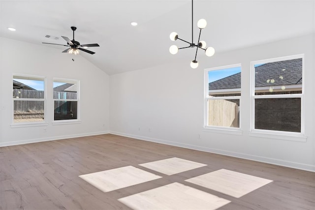 empty room with ceiling fan with notable chandelier, light hardwood / wood-style flooring, and vaulted ceiling