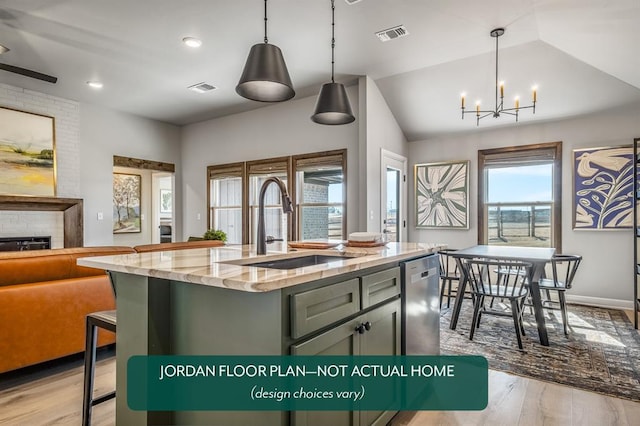 kitchen featuring light stone countertops, sink, light hardwood / wood-style flooring, decorative light fixtures, and a center island with sink