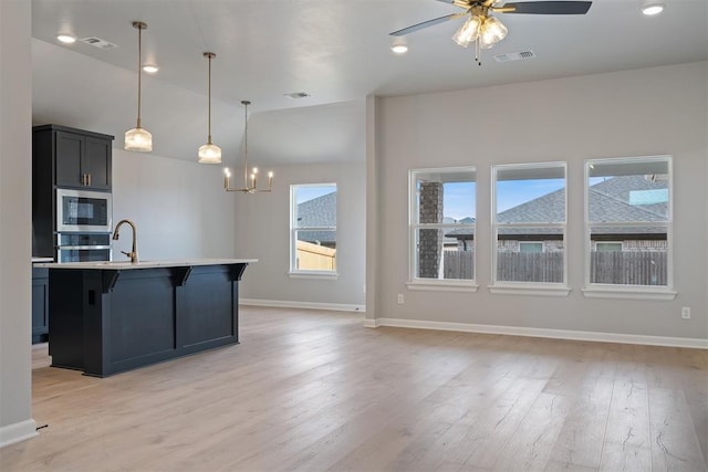 kitchen featuring pendant lighting, light hardwood / wood-style flooring, appliances with stainless steel finishes, an island with sink, and a kitchen bar