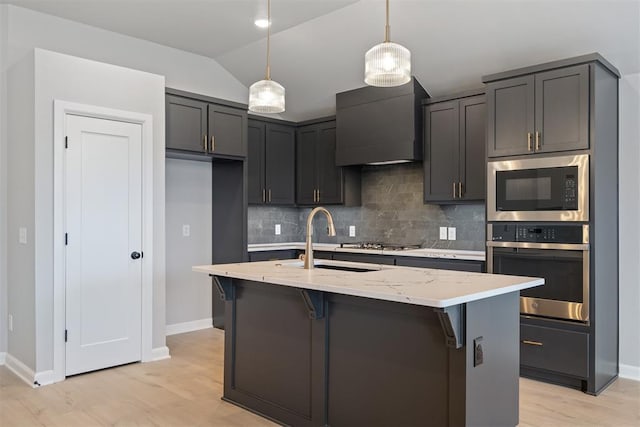 kitchen featuring sink, hanging light fixtures, an island with sink, stainless steel appliances, and light stone countertops