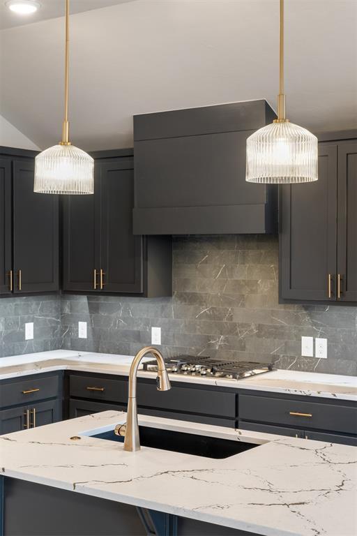 kitchen with pendant lighting, backsplash, light stone counters, and wall chimney exhaust hood